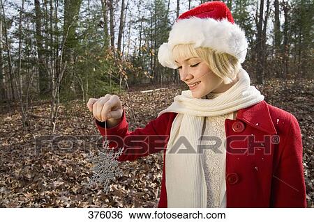 Young woman wearing a Santa hat and holding a decorative silver snowflake in the woods View Large Photo Image Stock Photograph - Young woman wearing a Santa hat and holding a decorative silver snowflake in the woods. Fotosearch