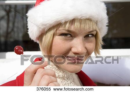 Stock Photography - Young woman wearing a Santa hat and holding a lollipop. Fotosearch