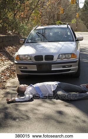 Man lying down on a road in front of a car View Large Photo Image Stock Photography - Man lying down on a road in front of a car. Fotosearch