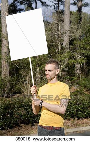 Stock Photo - Man standing on a roadside holding a blank placard. Fotosearch