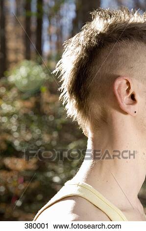 Stock Image - Side view of a man with a mohawk standing in the woods. Fotosearch