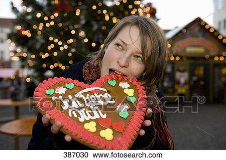 Stock Image - Woman biting a heart-shaped gingerbread cookie at a Christmas market, Berlin, Germany. Fotosearch