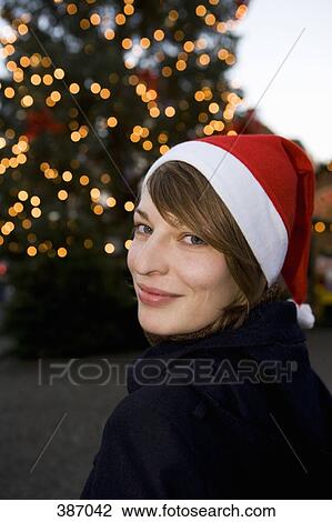 Woman wearing a Santa hat in front of a Christmas tree View Large Photo Image Stock Image - Woman wearing a Santa hat in front of a Christmas tree. Fotosearch