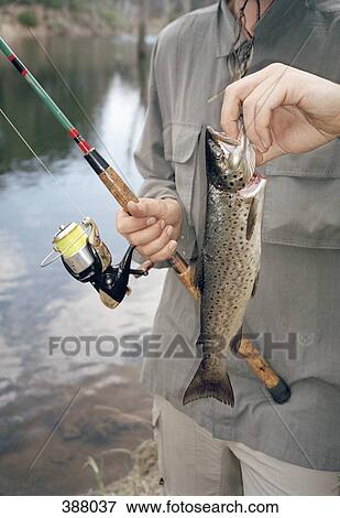 Stock Photo - Man holding a fishing rod and a Trout fish. Fotosearch