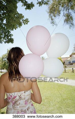 Woman standing in a park and holding a bunch of balloons View Large Photo Image Stock Image - Woman standing in a park and holding a bunch of balloons. Fotosearch
