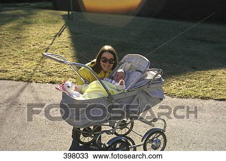 Stock Image - A mother posing next to her baby in a carriage on a sidewalk. Fotosearch