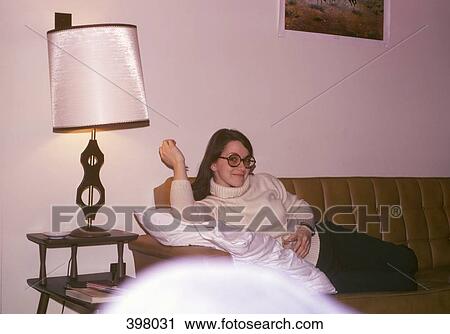 A woman reclining on a sofa in a living room View Large Photo Image Stock Image - A woman reclining on a sofa in a living room. Fotosearch