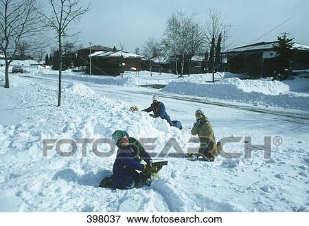 Three children playing in the snow next to a residential street View Large Photo Image Stock Photo - Three children playing in the snow next to a residential street. Fotosearch