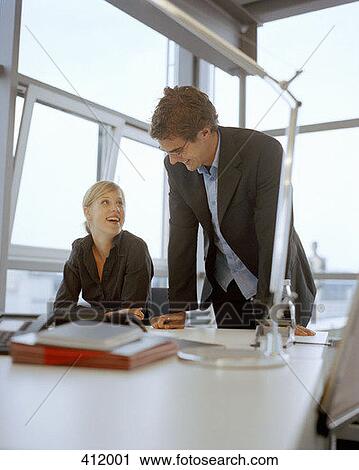 Stock Image - A young man and a young woman laughing in an office setting. Fotosearch