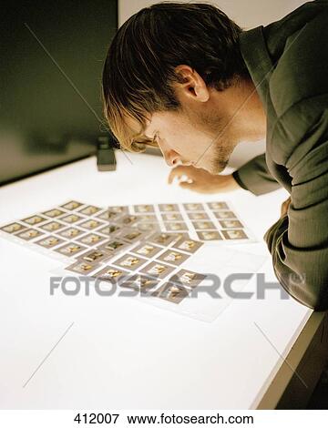 Stock Photo - Young man looking at slide transparencies on a light box. Fotosearch