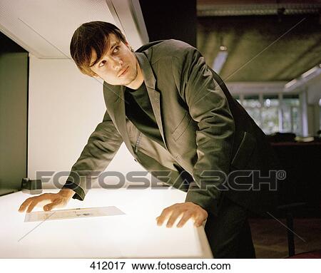 Stock Photo - Young man standing over a light box and looking away. Fotosearch