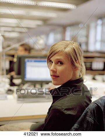 Young woman looking over her shoulder whilst sitting at an office desk View Large Photo Image Stock Image - Young woman looking over her shoulder whilst sitting at an office desk. Fotosearch