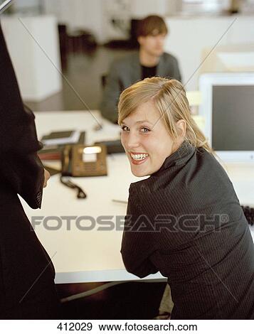 Stock Photo - Young woman looking over her shoulder whilst in a stylish office. Fotosearch