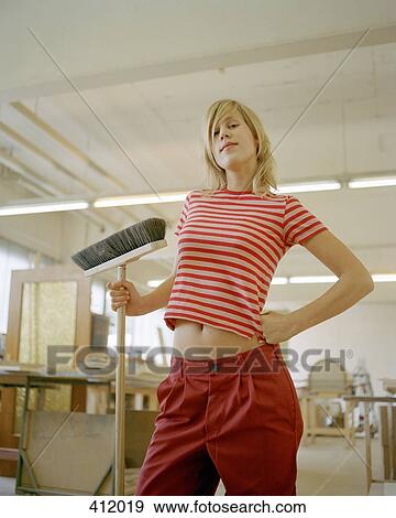 Young woman standing with a hand on her hip whilst holding a broom View Large Photo Image Stock Photo - Young woman standing with a hand on her hip whilst holding a broom. Fotosearch