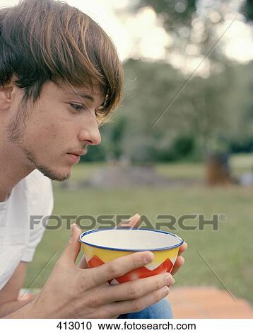 Stock Image - A young man drinking from a bowl. Fotosearch