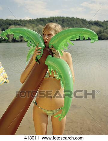 Stock Image - A young woman holding an inflatable palm tree by a lake. Fotosearch