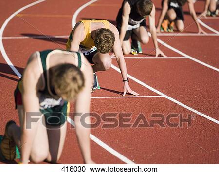 Stock Image - Group of male athletes in starting blocks on a running track. Fotosearch