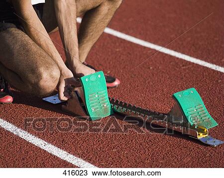 Stock Image - Man positioning starting blocks on a running track. Fotosearch