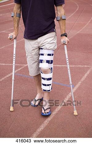 Stock Image - Man with his leg in a brace and using crutches. Fotosearch
