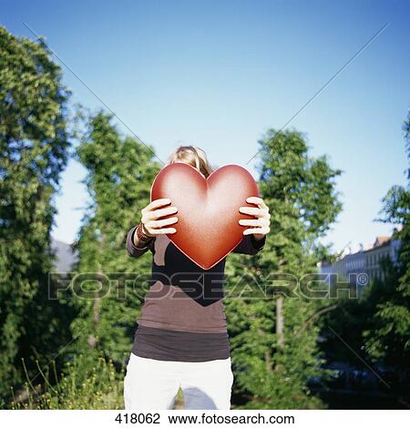 Woman holding a red heart in front of her face View Large Photo Image Stock Image - Woman holding a red heart in front of her face. Fotosearch