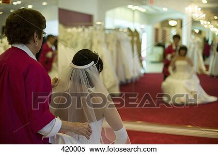 Stock Photography - Shop assistant helping a woman try on a wedding dress. Fotosearch