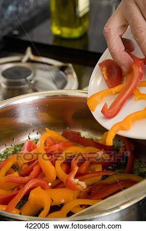 Stock Photography - A man putting sliced bell peppers into a saucepan. Fotosearch