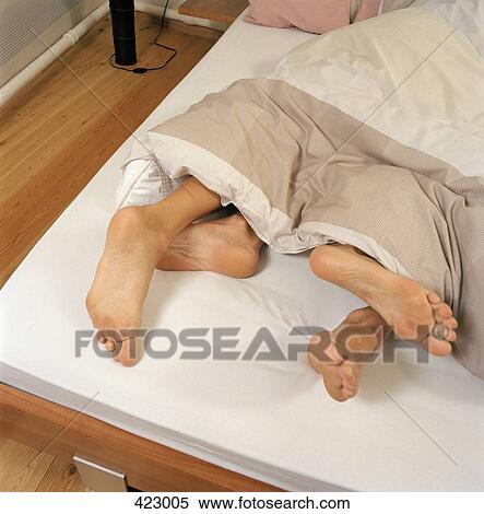 Stock Photography - Young couple lying in a bed with their feet poking out the end. Fotosearch