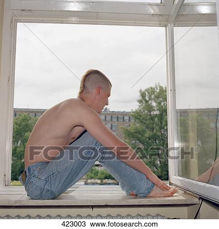 Stock Image - Young man sitting on the window sill of an open window. Fotosearch