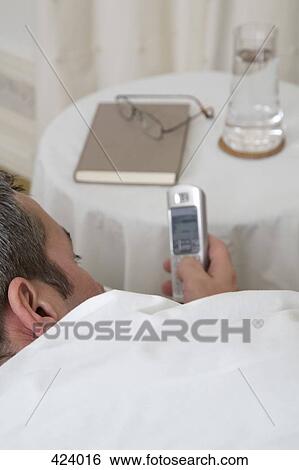 Businessman dialing on a cordless phone whilst lying in bed View Large Photo Image Stock Photograph - Businessman dialing on a cordless phone whilst lying in bed. Fotosearch
