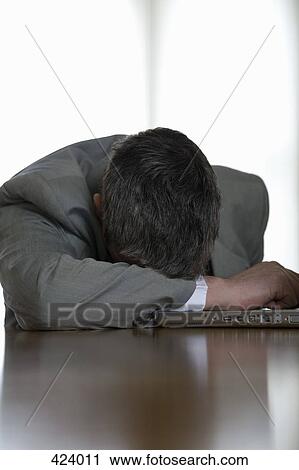 Businessman resting on his laptop at a desk View Large Photo Image Stock Image - Businessman resting on his laptop at a desk. Fotosearch
