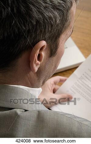Businessman sitting at a table reading a document View Large Photo Image Stock Photo - Businessman sitting at a table reading a document. Fotosearch
