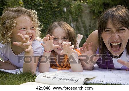 Stock Photo - A woman and two girls growling whilst lying down in a backyard. Fotosearch