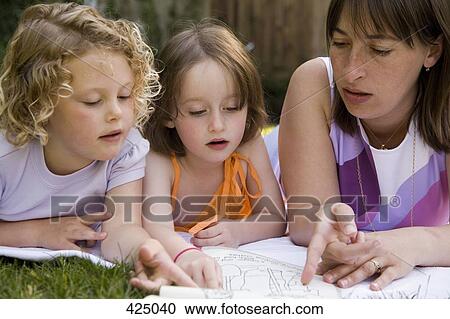 A woman and two girls lying down in a backyard and reading a book together View Large Photo Image Stock Image - A woman and two girls lying down in a backyard and reading a book together. Fotosearch