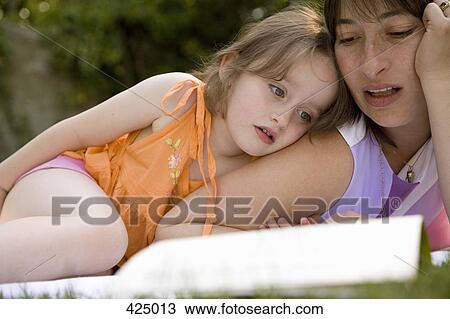 Stock Image - Mother and daughter lying down and reading a book together in a backyard. Fotosearch