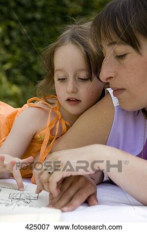 Mother and daughter lying down and reading a book together in a backyard View Large Photo Image Stock Photo - Mother and daughter lying down and reading a book together in a backyard. Fotosearch