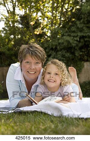 Stock Photography - Mother and daughter lying down and reading a book together in a backyard. Fotosearch
