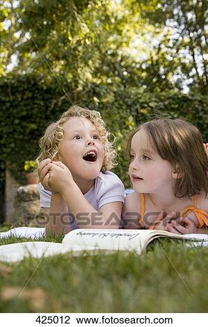 Stock Image - Two girls lying down side by side in a backyard. Fotosearch