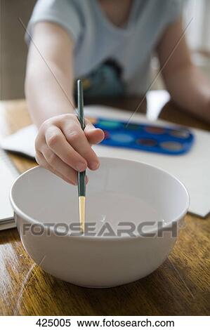 Stock Photography - Young girl rinsing a paintbrush in a bowl of water. Fotosearch