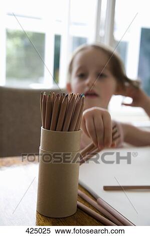 Young girl sitting at a table and reaching for colored pencils View Large Photo Image Stock Photography - Young girl sitting at a table and reaching for colored pencils. Fotosearch