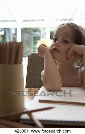 Stock Image - Young girl sitting at a table with a sketch pad and colored pencils. Fotosearch