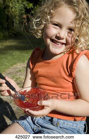 Stock Photo - Young girl sitting in a backyard eating jello. Fotosearch