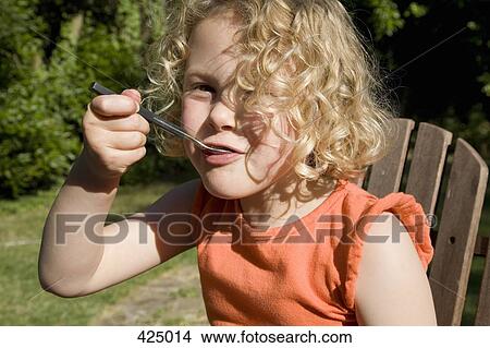 Young girl sitting in a backyard with a spoon in her mouth View Large Photo Image Picture - Young girl sitting in a backyard with a spoon in her mouth. Fotosearch