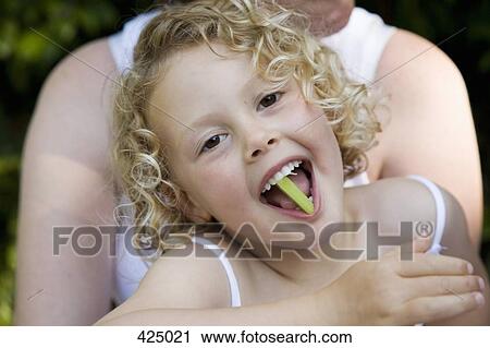 Young girl sitting on her mother's lap with a piece of celery in her mouth View Large Photo Image Stock Image - Young girl sitting on her mother's lap with a piece of celery in her mouth. Fotosearch