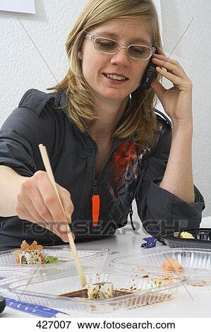 Woman easting sushi at desk and talking on mobile phone View Large Photo Image Stock Photo - Woman easting sushi at desk and talking on mobile phone. Fotosearch