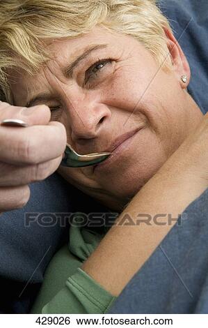 Stock Photograph - A woman taking medicine from a spoon. Fotosearch