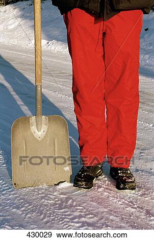 Stock Photo - Man standing next to a shovel in the snow. Fotosearch