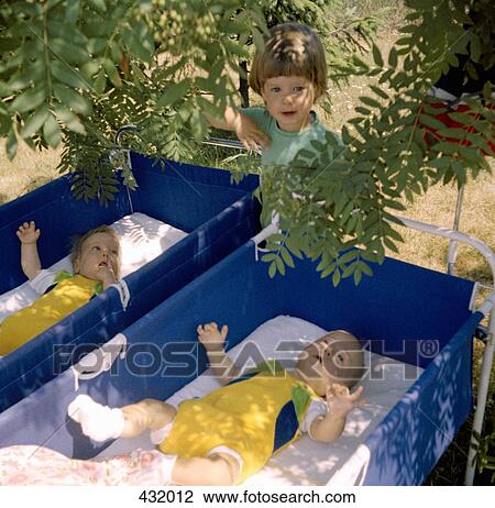 Stock Image - Child standing next to two baby cribs. Fotosearch