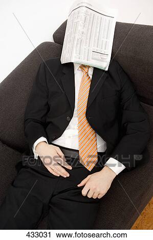 Stock Image - Businessman lying down on a sofa with a newspaper over his head. Fotosearch