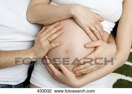 Stock Image - Midsection of a pregnant couple lying down together. Fotosearch