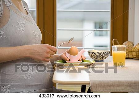 Pregnant woman cracking a boiled egg at breakfast View Large Photo Image Stock Photo - Pregnant woman cracking a boiled egg at breakfast. Fotosearch
